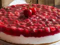 Pyszny sernik na zimno z wiśniami w galaretce, ozdobiony dwoma świeżymi wiśniami na wierzchu. Idealny na letnie popołudnie.