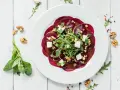 Eleganckie carpaccio z buraka z rukolą, orzechami włoskimi i kostkami sera feta na białym talerzu.