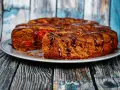 Pyszne ciasto z malinami, polane czekoladą, na talerzu na tle drewnianej deski.