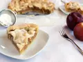 Pyszna tarta z jabłkami, posypana cukrem pudrem, czeka na widelcu. Obok leżą świeże jabłka.