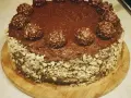 Pyszny tort ferrero rocher, oblany czekoladą i ozdobiony orzechami oraz kulkami.