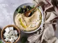 Pyszna pasta z ciecierzycy z fetą, oliwkami i ziołami, podana z serem feta w drewnianej misce.