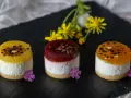 Trzy miniaturowe ciasta bez pieczenia: dwa z żółtą galaretką, jedno z czerwoną. Udekorowane kwiatami i czekoladą.