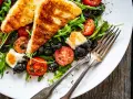 Pyszna sałatka z grillowanym halloumi, pomidorkami koktajlowymi i czarnymi oliwkami na talerzu.