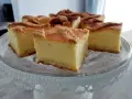 Pyszny sernik na kruchym spodzie, pokrojony na kwadratowe kawałki, prezentuje się apetycznie na szklanej paterze.