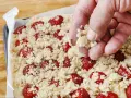 Ręka posypuje kruszonką ciasto z truskawkami. Zapowiada się pyszne ciasto z truskawkami i kruszonką!