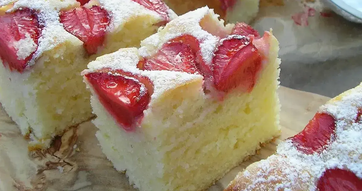 Puszyste ciasto na maślance z kawałkami truskawek, posypane cukrem pudrem. Idealne na letnie popołudnie.