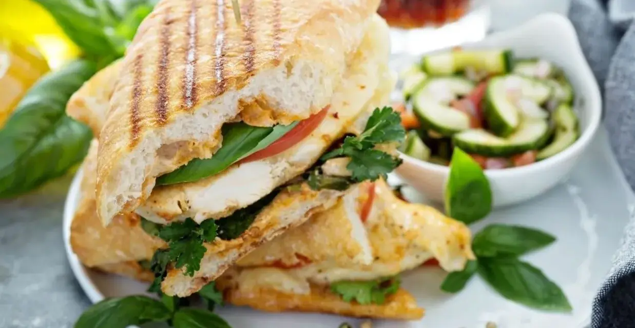 Pyszne panini z kurczakiem, pomidorem i bazylią, podane z sałatką z ogórka. Idealne na lekki posiłek.