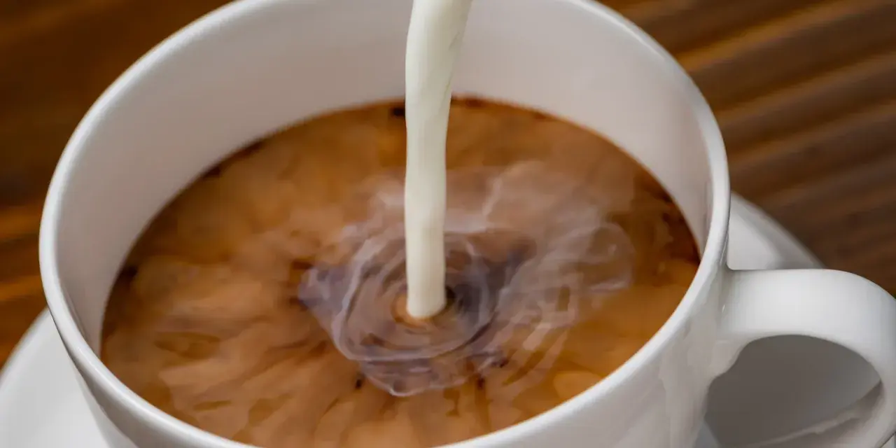 Biała filiżanka kawy, do której wlewane jest mleko. Zastanawiasz się nad mleko owsiane kcal?