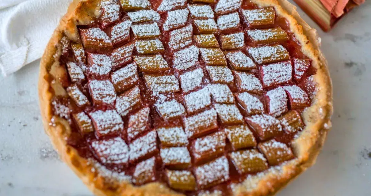 Tarta z rabarbarem posypana cukrem pudrem, obok łodygi rabarbaru.