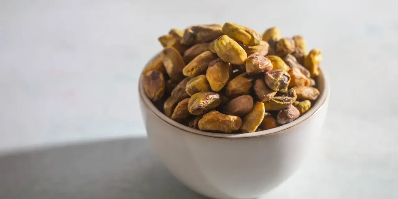 Misternie ułożone pistacje w miseczce. Czy pistacja to orzech? Botanicznie to pestkowiec, ale kulinarnie często traktowany jak orzech.