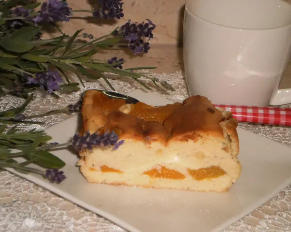 Pyszny sernik z brzoskwiniami, udekorowany gałązką lawendy, czeka na kawę.