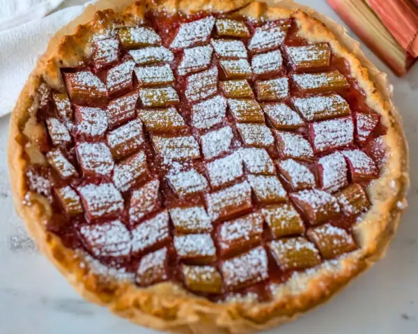 Tarta z rabarbarem posypana cukrem pudrem, obok łodygi rabarbaru.
