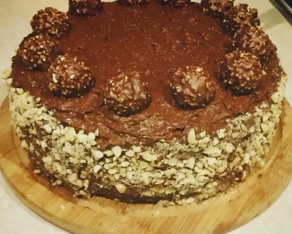 Pyszny tort ferrero rocher, oblany czekoladą i ozdobiony orzechami oraz kulkami.