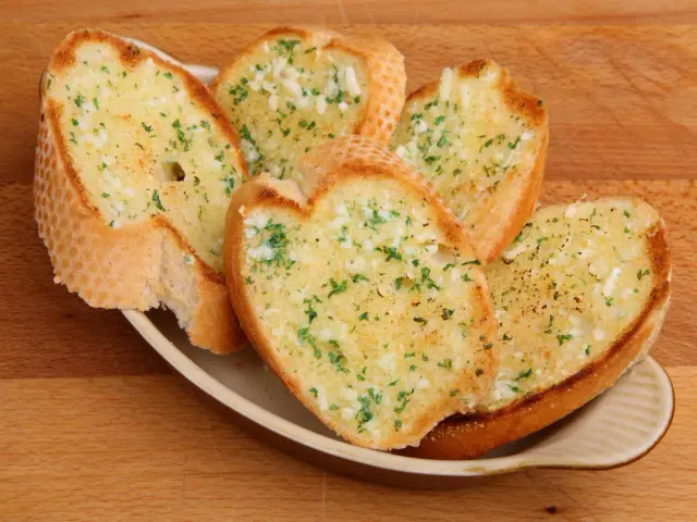Chrupiące grzanki czosnkowe, idealne przekąski na ognisko. Aromatyczne, posypane natką pietruszki, czekają na rozgrzanie przy ogniu.
