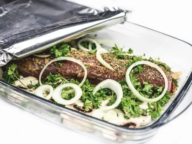 Mięso w naczyniu żaroodpornym, przykryte folią aluminiową. Cebula, pietruszka i przyprawy dodają smaku. Folia aluminiowa która strona do pieczenia?