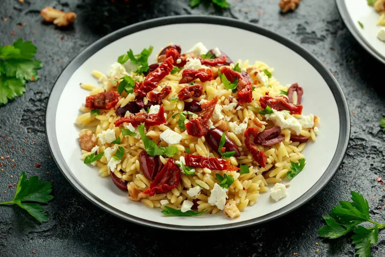 Pyszna sałatka z makaronem orzo, suszonymi pomidorami, oliwkami, fetą i natką pietruszki.