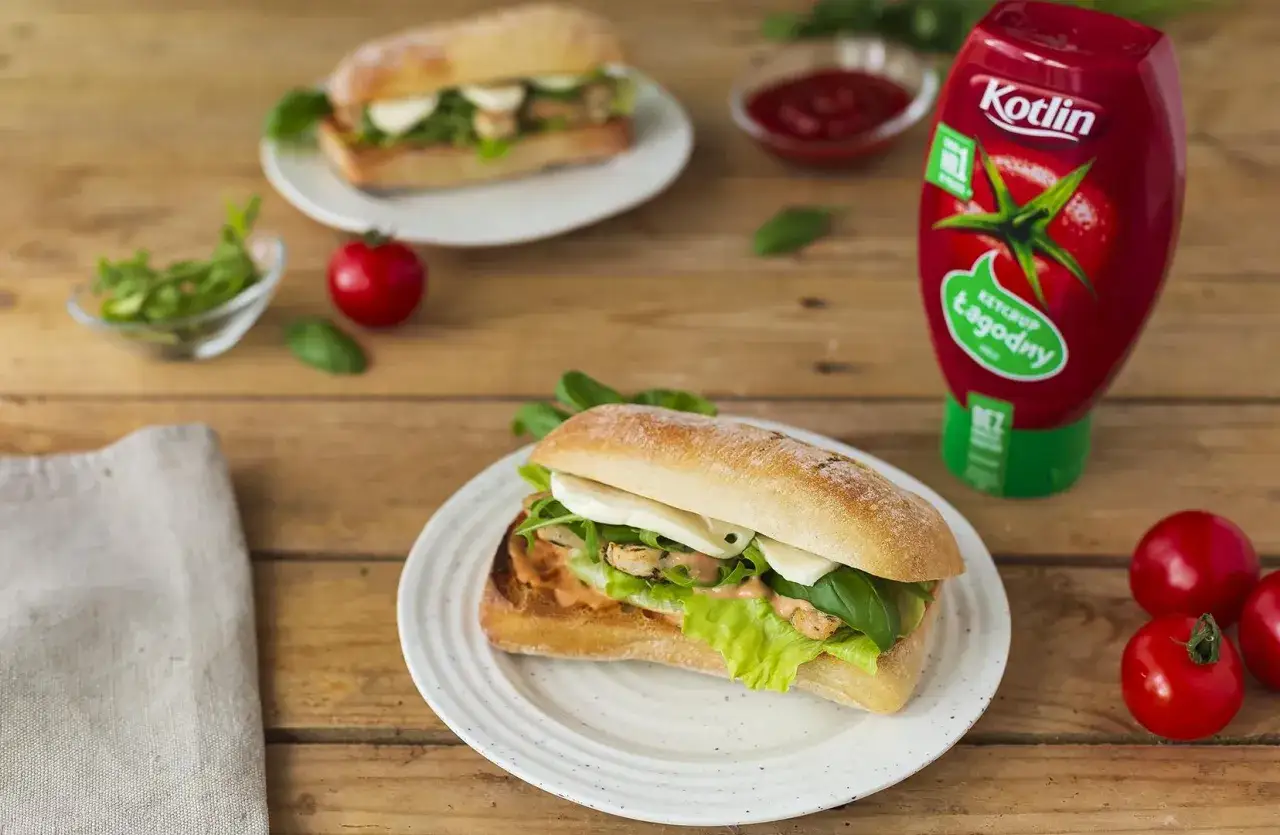 Pyszne panini z kurczakiem, sałatą i mozzarellą, obok butelka ketchupu Kotlin i pomidorki.