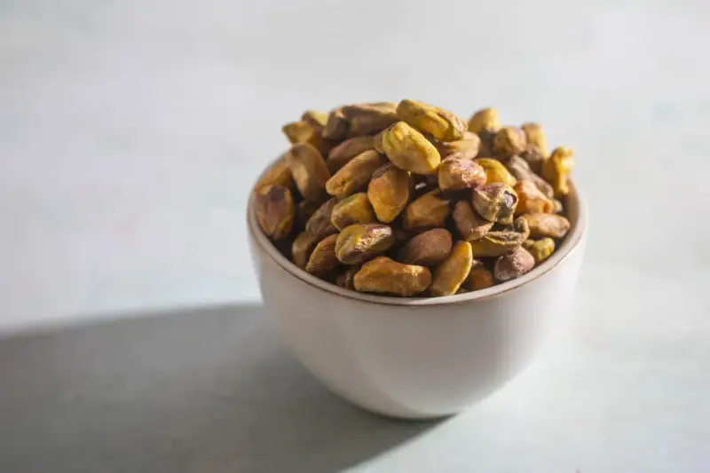 Misternie ułożone pistacje w miseczce. Czy pistacja to orzech? Botanicznie to pestkowiec, ale kulinarnie często traktowany jak orzech.